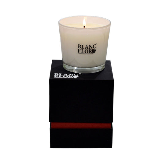 A white luxury fragranced candle named 'The Rose', placed on a black gift box with a red ribbon.