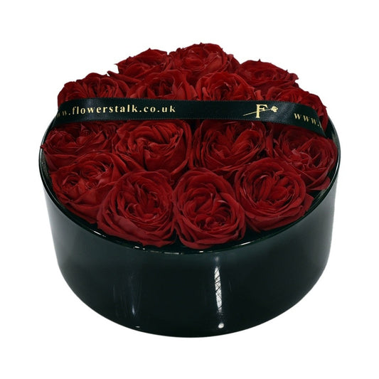 A glass container with preserved red roses, sealed with a black lid.